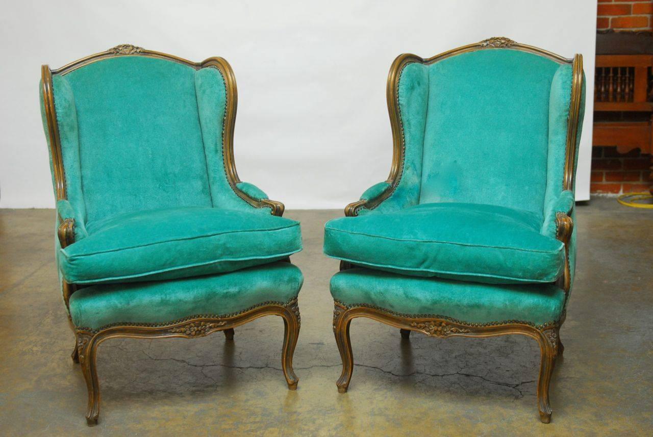 Impressive pair of French wingback armchairs made in the Louis XV taste featuring turquoise velvet upholstery with thick down filled cushion and finely carved frames with extended wings. Supported by cabriole legs and finished with brass nail head