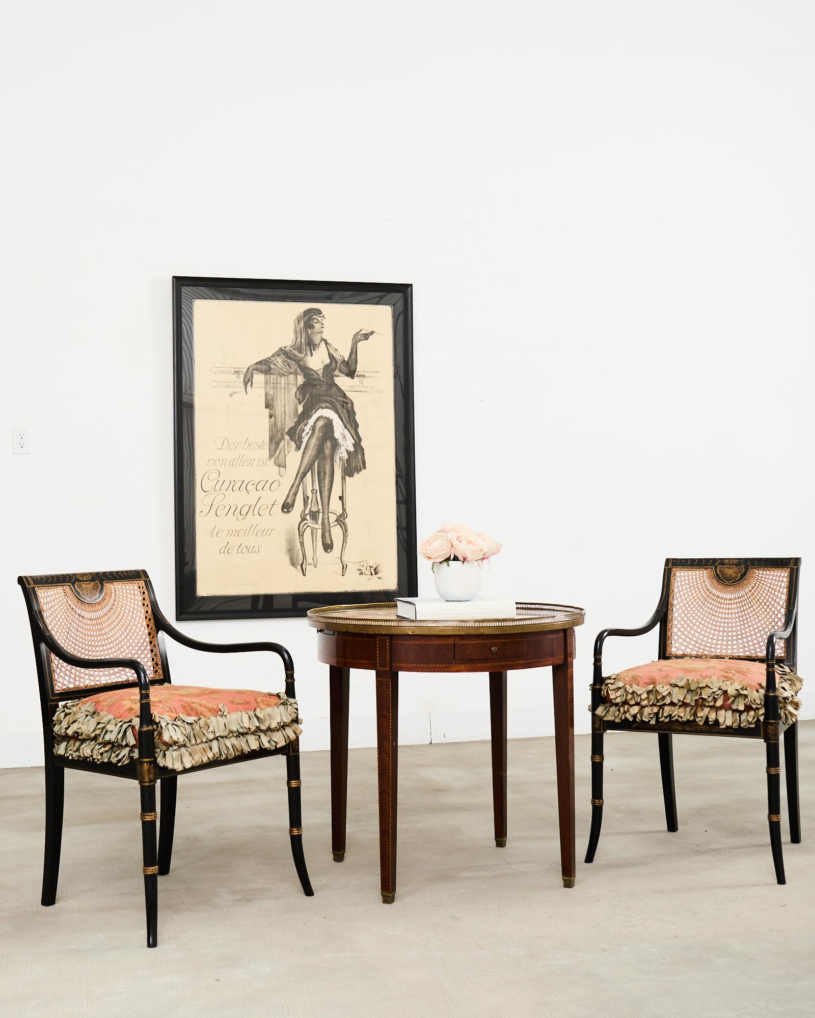 Striking pair of matching black lacquer ebonized English elbow armchairs crafted in the Regency taste. The chairs feature a beech frame with a caned seat and back having large gracefully curved arms. The lacquered frames have decorative parcel gilt