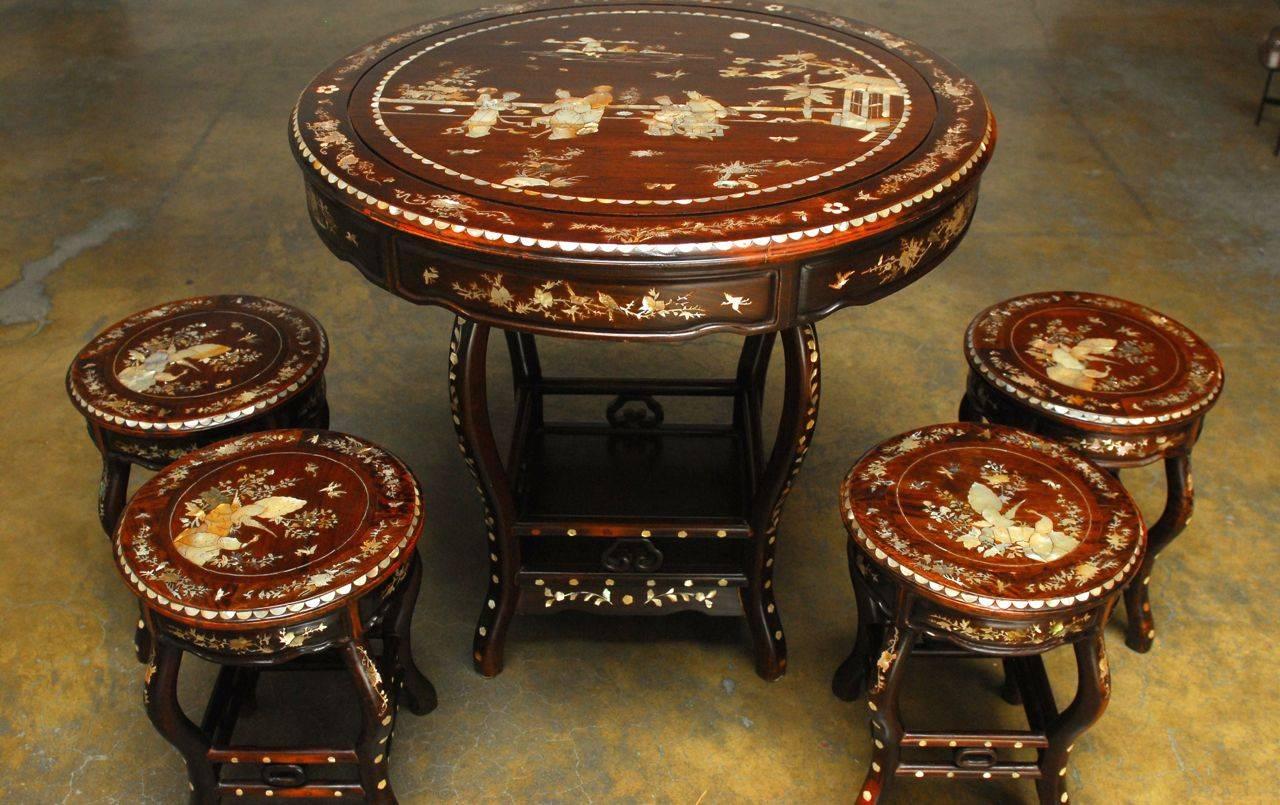 Striking intricately inlaid tea table, crafted from high quality hongmu rosewood. This tall table features a large scene of Chinese beauties relaxing in an outdoor court with a pond. Inlay continues throughout the legs and frame, with four stools