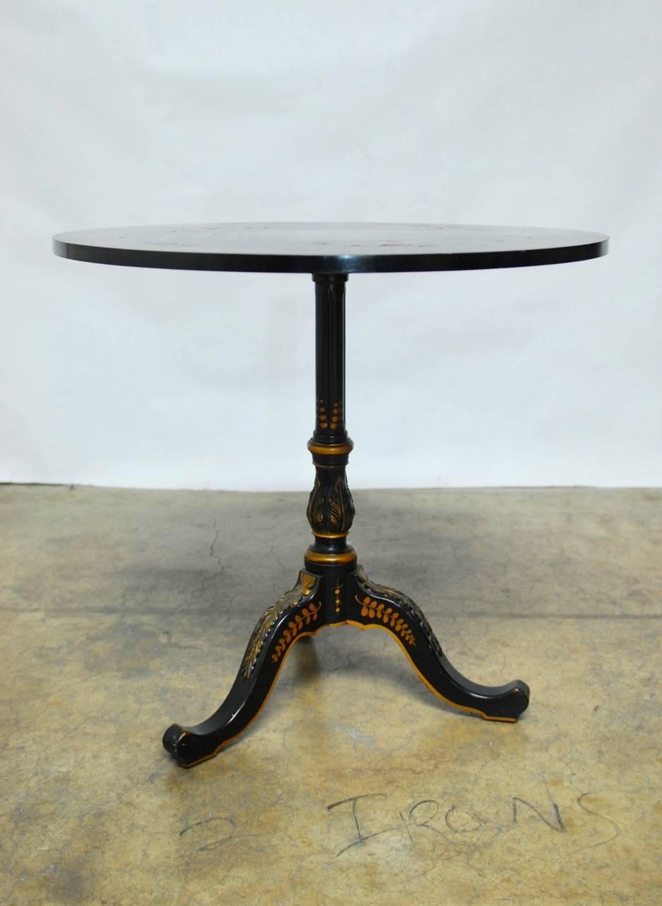 Charming round tripod tea table made in the Georgian style and featuring a black lacquer chinoiserie decoration. Hand-painted in gilt with an Asian motif by W. J. Sloane. Supported by a turned column and a tripod base decorated with acanthus