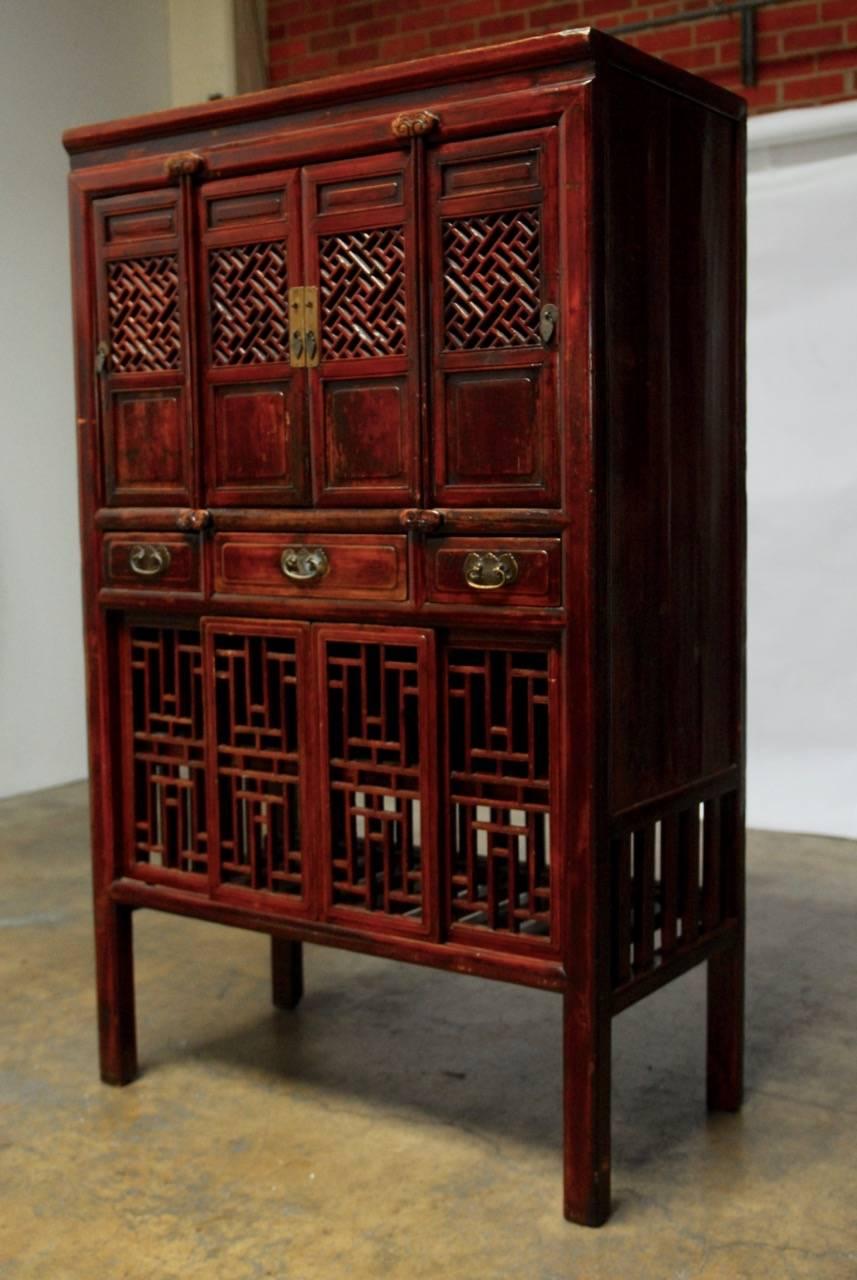 Impressive Chinese lacquered kitchen cabinet featuring decorative carved geometric lattice doors on top and bottom. The cabinet was produced with mortise and tenon joinery and has four small doors on top with wood hinges. The middle has three
