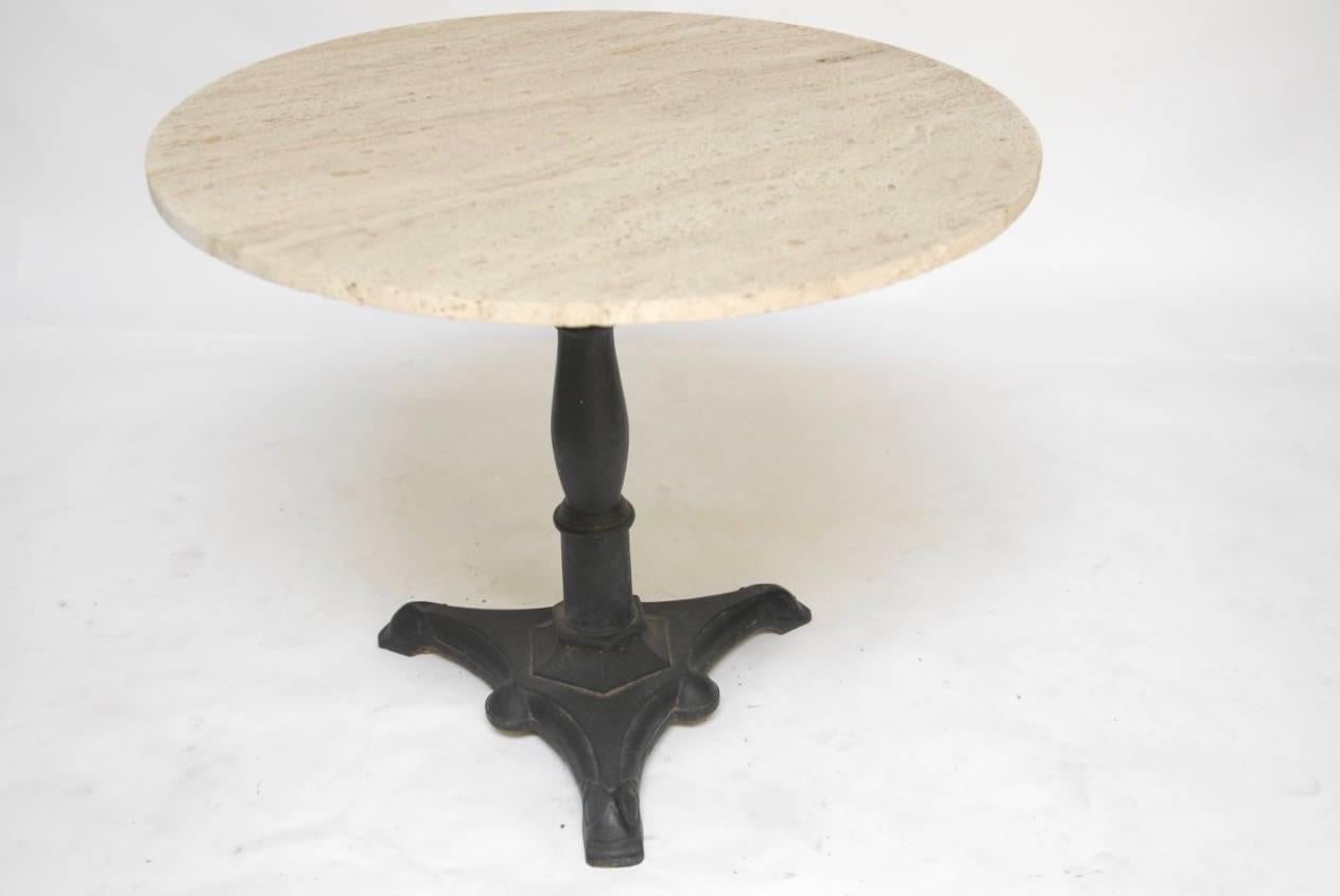 Stunning French round travertine bistro table with a baluster form cast iron pedestal. The pedestal is supported by a tripod base with geometric designs in the Art Deco taste. The table features a thick 1