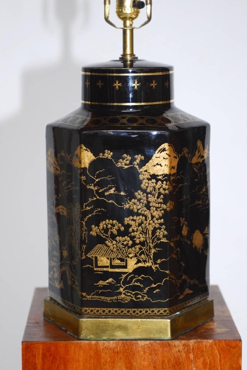 Stylish Chinese porcelain tea canister style table lamp featuring a gilt painted Asian themed decoration and a hexagon shape. Supported by a conforming brass metal base and brass hardware with a prosperity finial. Includes harp and finial with no