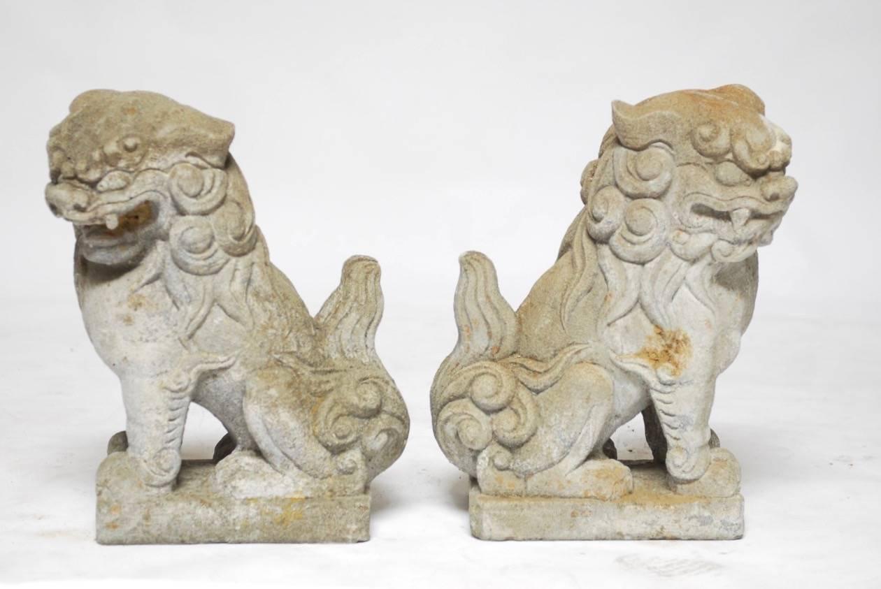 Fierce pair of Chinese molded stone guardian foo lions or foo dogs. Each with expressive faces depicted seated on a plinth with wavy tails and curls.

 