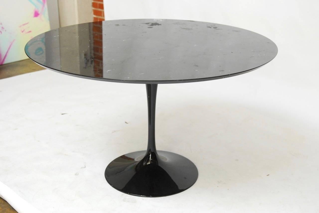 Dramatic Mid-Century Modern tulip dining table featuring a large round black marble top with white veining. Supported by a cast iron base finished in a black lacquer. Designed by Eero Saarinen for Knoll, this high quality redux has a swivel top and