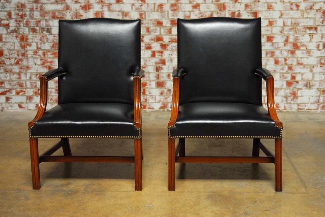 Classic pair of black leather and mahogany Gainsborough wingback library chairs made in the George III taste, decommissioned from Universal Studios property department in Hollywood CA. Once part of their movie set inventory, they now feature a new
