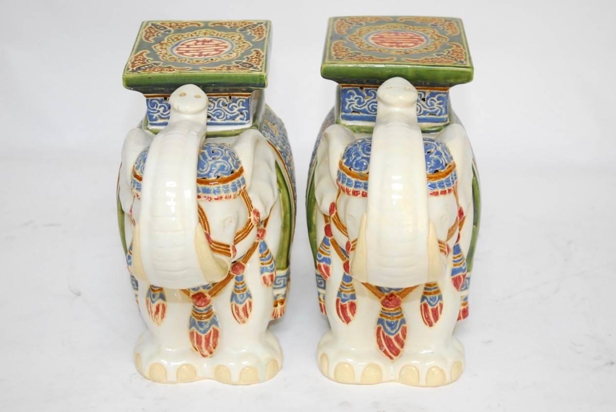 Charming pair of Chinese glazed elephant ceramic garden stools or drink tables featuring colorful pierced fretwork design outfits. Depicted trunks up for good luck with prosperity symbols on the seats and sides.
