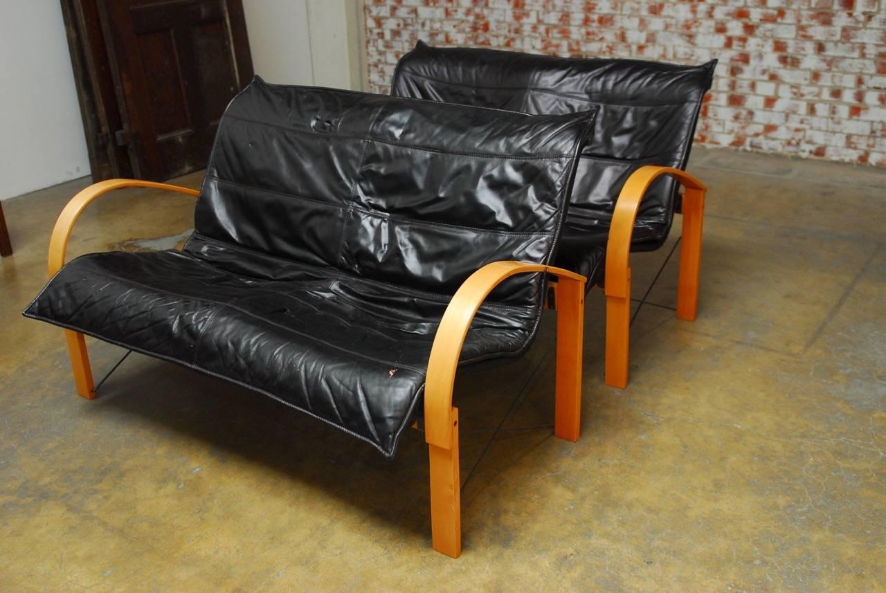 Ergonomic pair of Mid-Century Scandinavian black leather sofas or settees featuring a bentwood frame with curved arms and hidden metal supports. Soft and supple leather one piece slip covers attach for a perfect seating angle. Good condition with