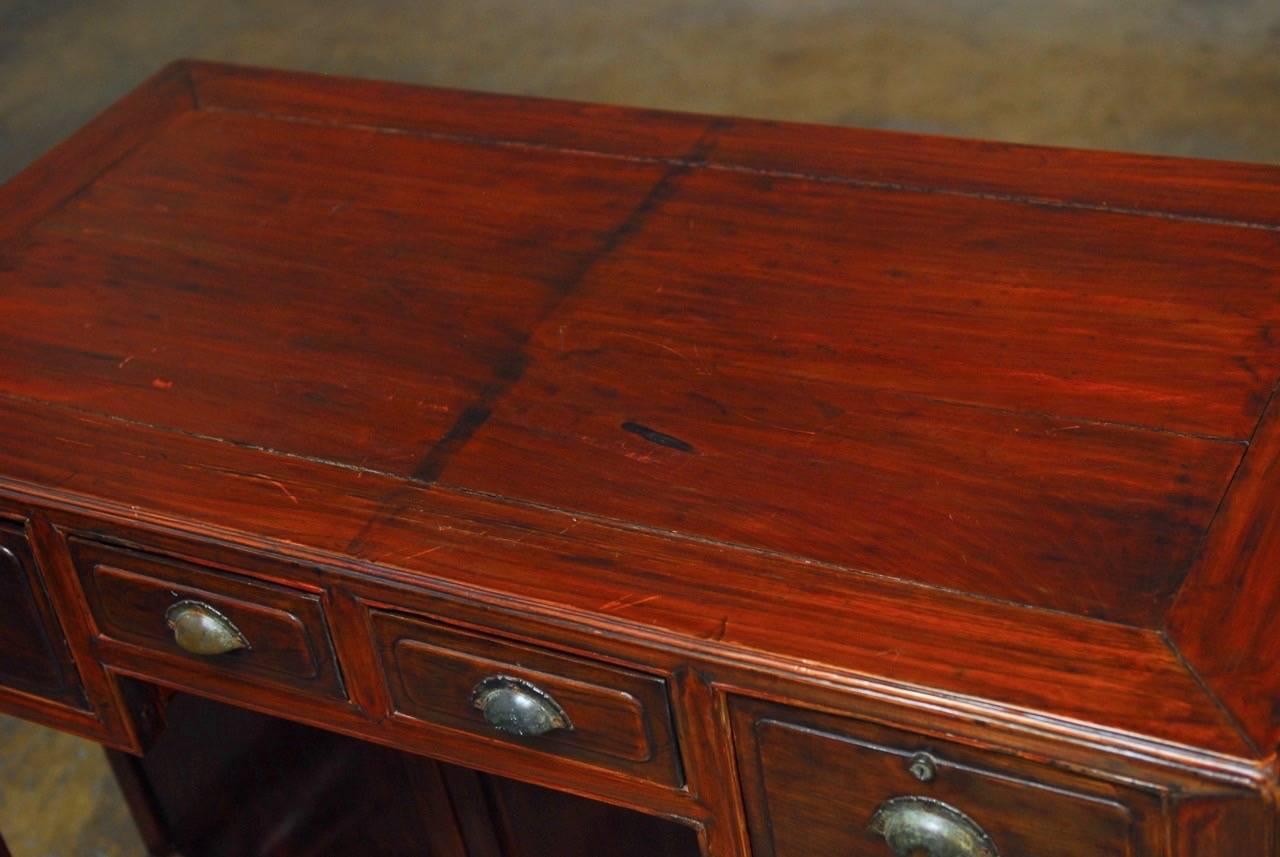 Distinctive Chinese red lacquered four-drawer desk featuring a carved cracked-ice lattice footrest. The case has been finished with decorative panels on all sides that showcase the beautifully grained hardwood and the drawers have brass pulls. The