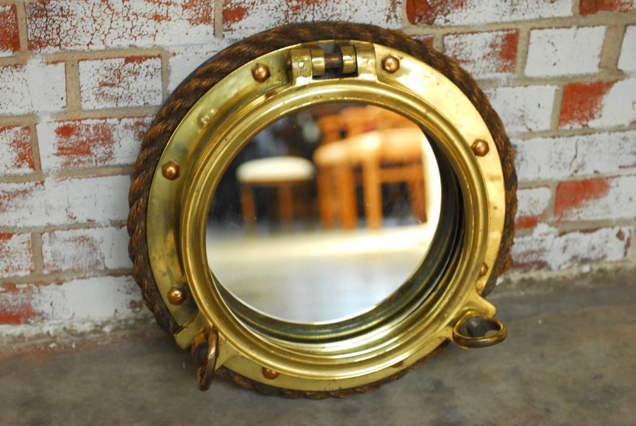 Rare British Royal Navy solid brass ships porthole window converted to a mirror and mounted on a wood disk with hanging hardware. Features a thick nautical rope border and fully functioning window latches.