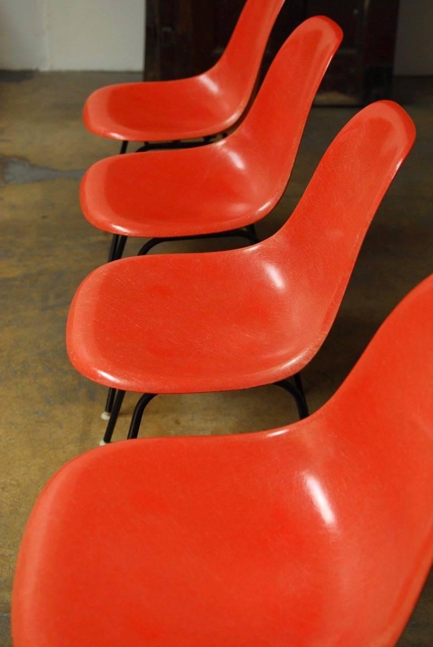 Iconic Mid-Century Modern set of four Charles and Ray Eames design for Herman Miller fiberglass shell chairs featuring a bright orange finish. All chairs have the original Herman Miller Furniture Company stamp on bottom from Zeeland, Michigan.