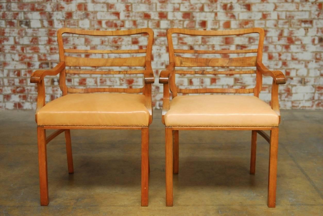 Distinctive pair of Mid-Century Modern English library chairs with leather upholstery and brass nailhead borders. These library chairs have a hardwood frame decorated with a mahogany veneer of beautifully grained wood. The generous seat has