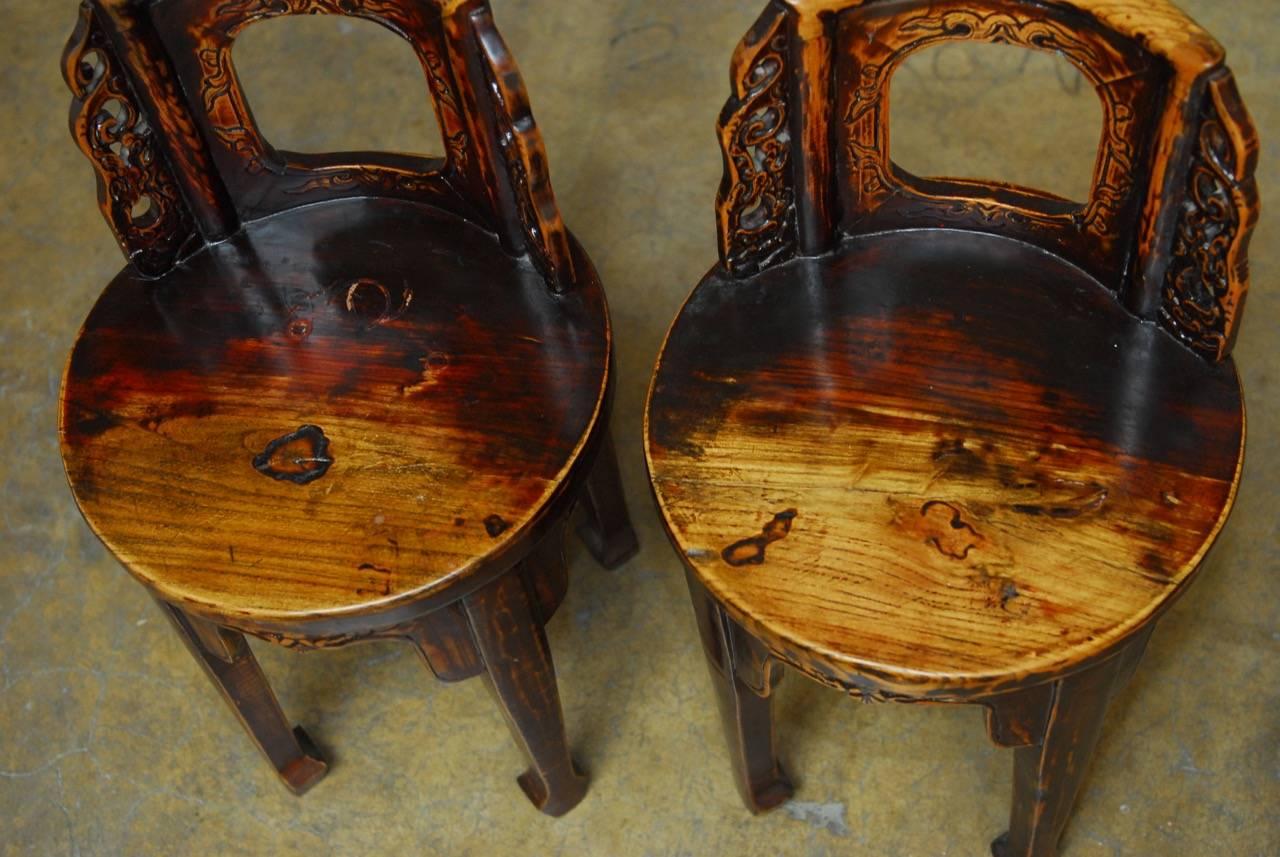 Distinctive pair of Chinese hand-carved round stools with back supports. These small stools have a vintage lacquer finish that is worn and faded showing the natural wood finish. The construction joinery is tight and the stools have decorative
