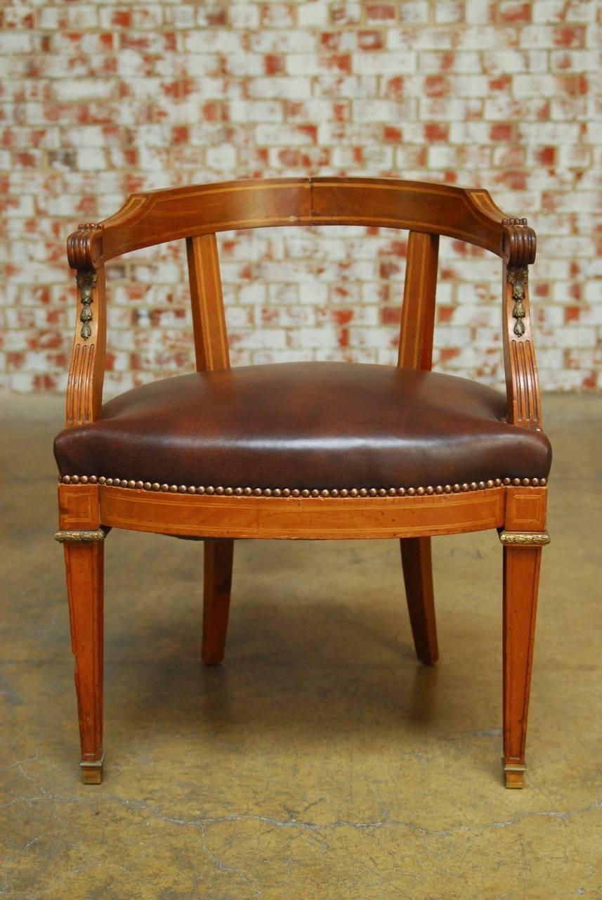 Handsome neoclassical French Empire barrel-back armchair constructed from mahogany with decorative satinwood inlay. Adorned with delicate ormolu accents of bell flowers on the reeded arm supports that conjoin to a curved crest rail. Features a rich