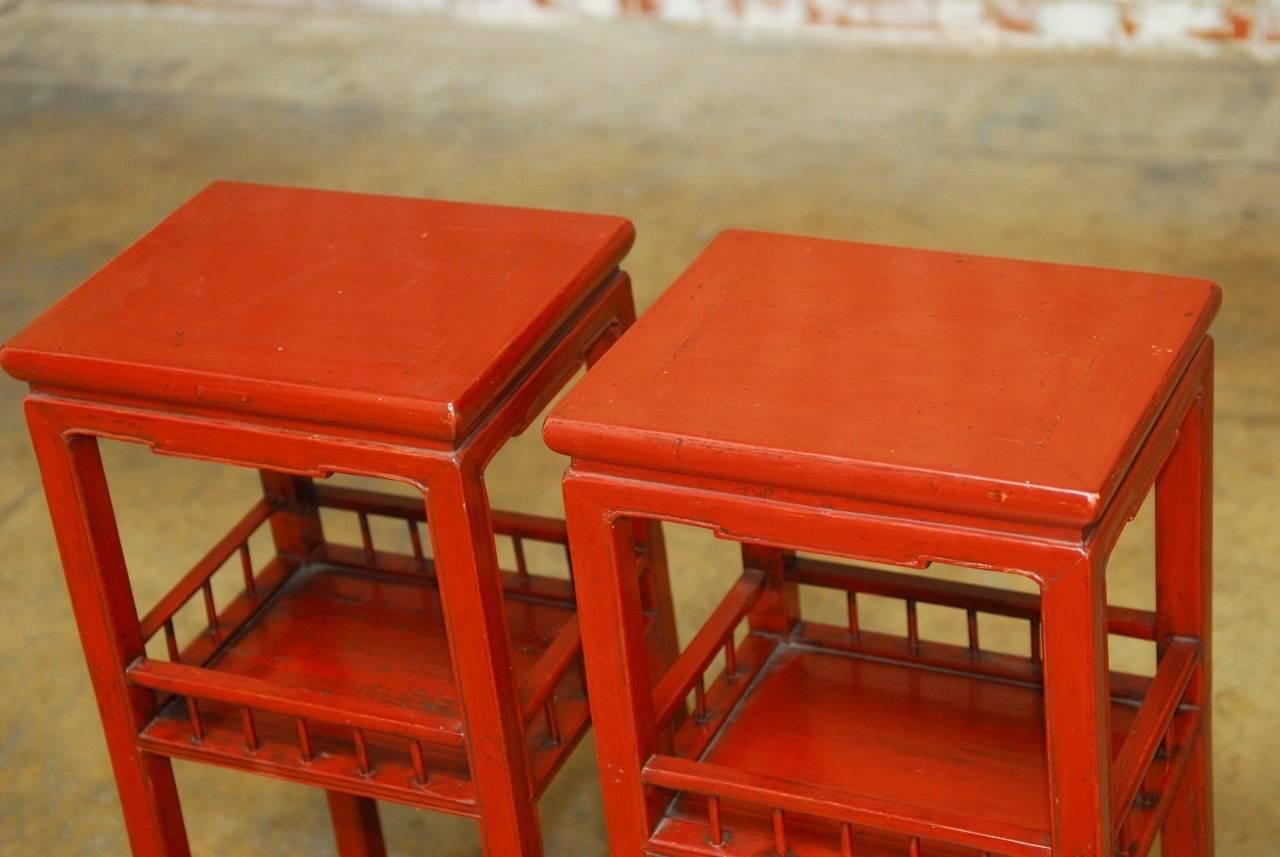 Colorful Chinese carved red lacquered pedestal tables featuring a floating top panel and a lower galleried shelf. Constructed with old world mortise and tenon joinery. Supported by square legs with box stretchers on bottom.