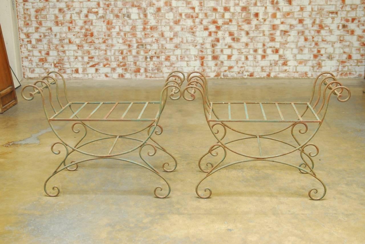 Stylish pair of Hollywood Regency wrought iron Curule benches made in the Neoclassical taste. Featuring an X-form design with scrolled arms and feet. The seats measure 25 inches wide and 18 inches deep and do not have cushions. These benches are