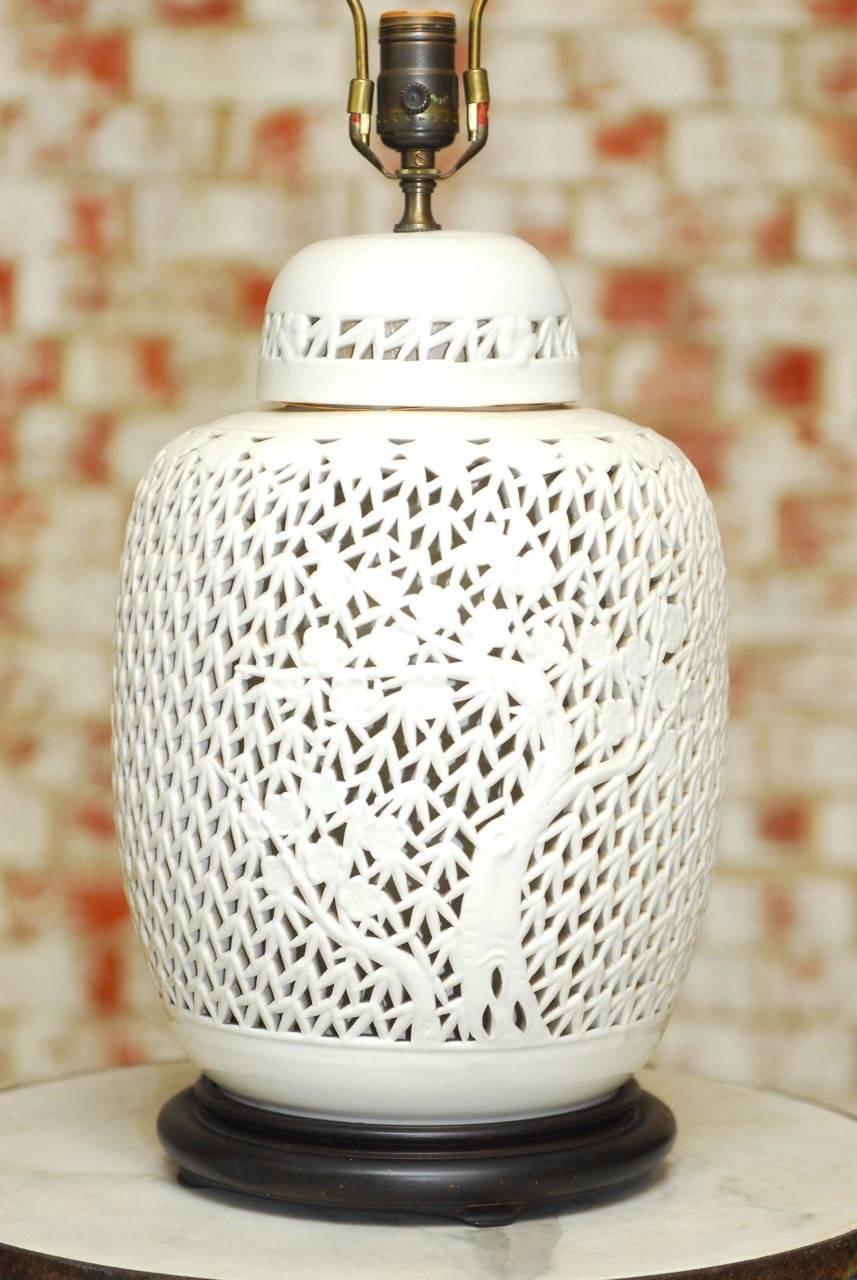 Large Mid-Century Modern porcelain blanc de chine table lamp featuring an urn shaped form with a pierced fretwork of foliate and cherry blossoms. Topped with a lid and brass hardware. This table lamp illuminates to showcase the intricate design