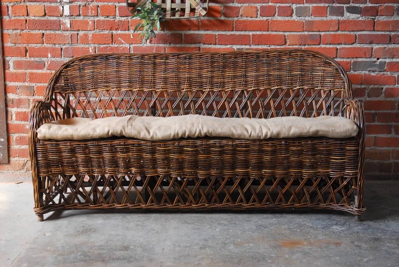 Distinctive organic rattan and stick wicker settee made in the bar harbor style. Constructed from a natural rattan frame with graceful braided arms and back. Decorated with a open fretwork back and apron and topped with a thin burlap seating
