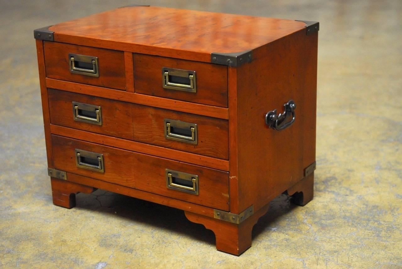 Diminutive campaign style chest of drawers or bachelor's dresser by Hekman. Fronted by four drawers lined with felt. Brass mounted protectors and pulls supported by shaped feet. Decorated on top with matched flame veneer mahogany. 