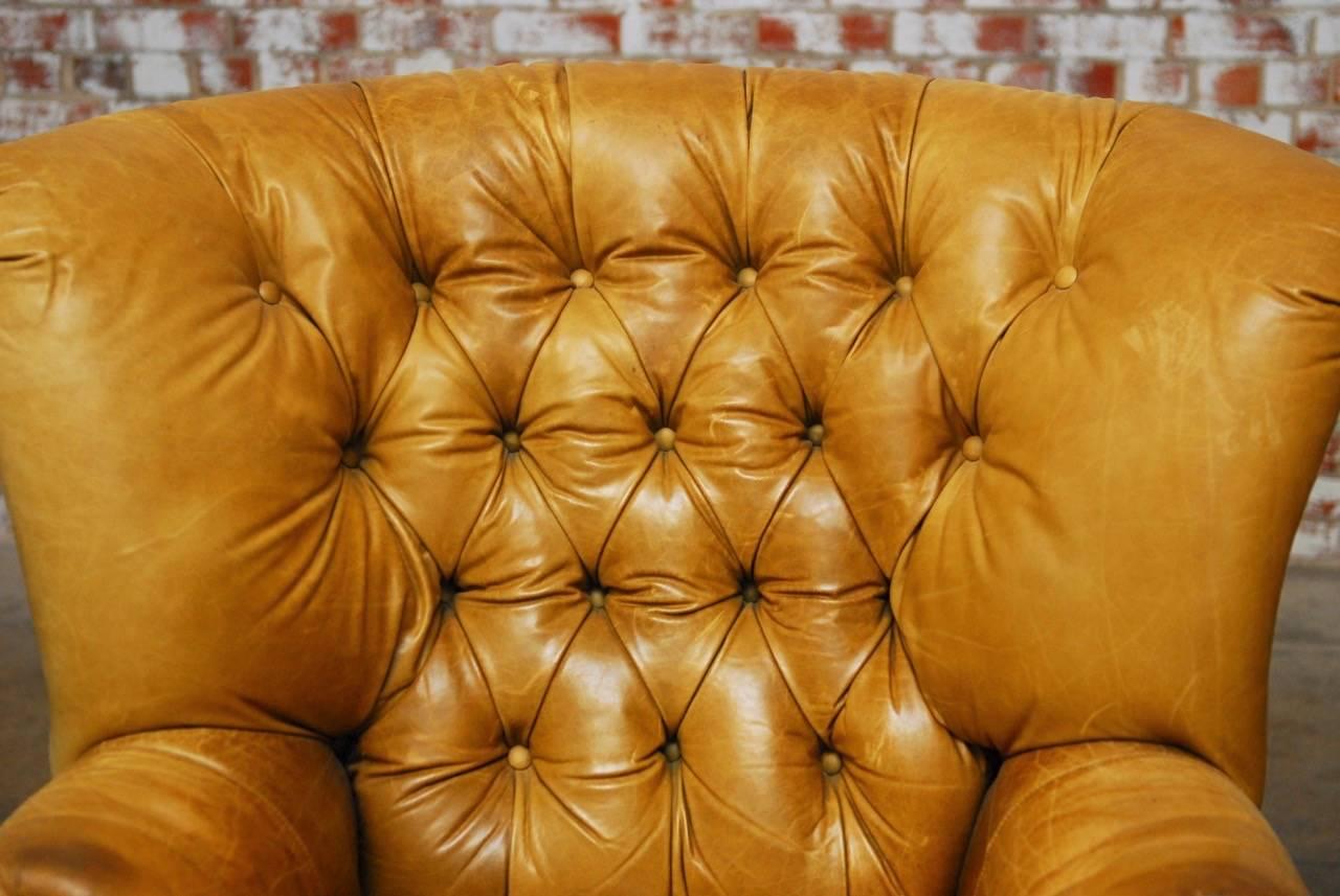 Grand English tufted leather Chesterfield library chair or wing chair made in the Georgian taste. Perfectly time faded and worn from an original olive green into a rich dijon color with a gorgeous patina. Constructed on a grand scale with generous
