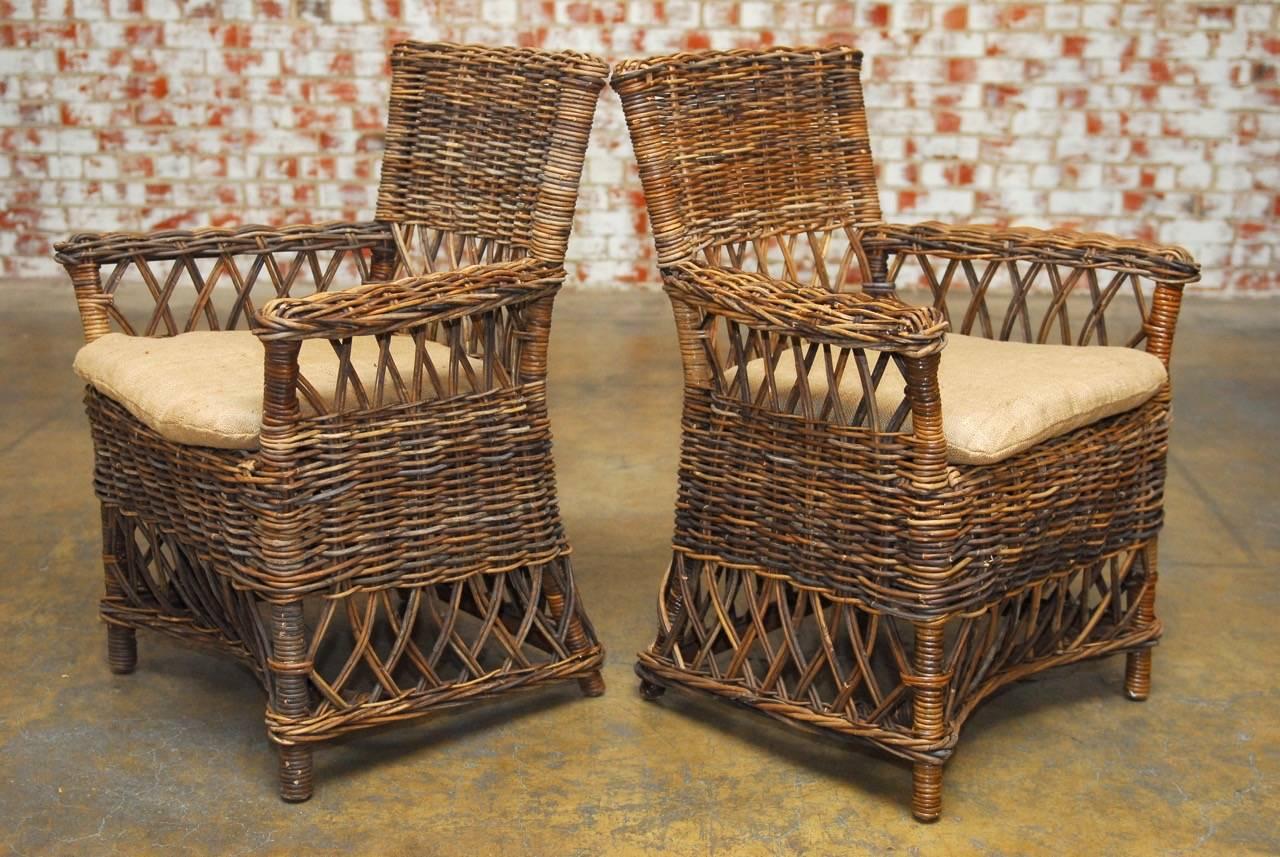 Organic pair of woven stick wicker armchairs constructed from natural twig frames. Features an open fretwork back and apron with braided arms. Upholstered with a thin natural burlap seat cushion. Strong and stable with a very comfortable seating