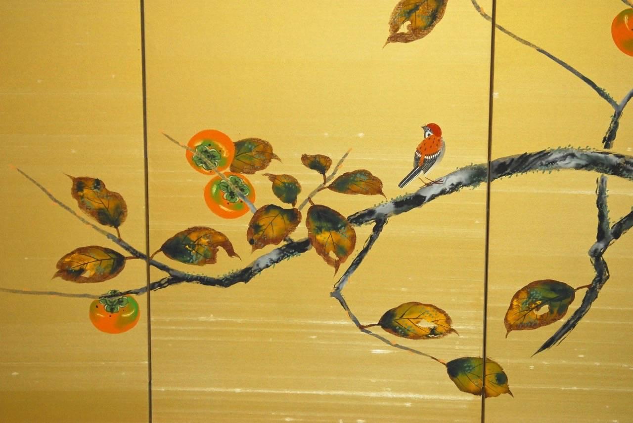 Exceptional Japanese silk four-panel folding screen or byobu screen featuring a fruiting persimmon branch. Decorated with foliate, ripe fruit, and a red bird. The screen has a richly textured silk ground as if raw in a gold color which makes the