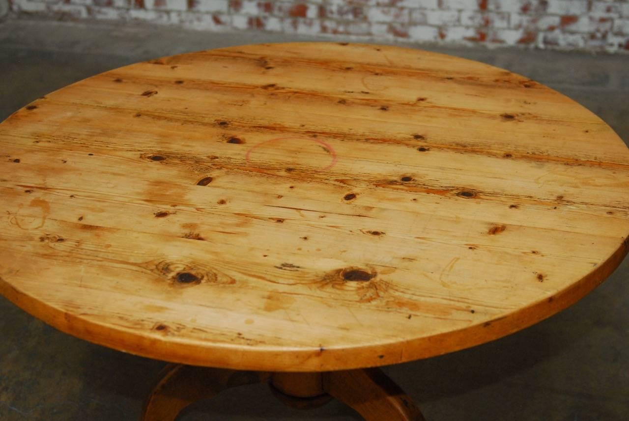 Gorgeous 19th century rustic french country round pine dining table featuring a thick 1.75 inch pine plank top. Beautifully distressed and supported by a turned pedestal with a tripod base. Soft pine patina for a perfectly worn farmhouse style.