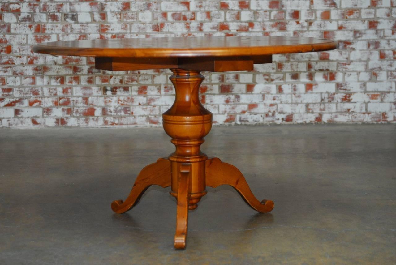 Handsome English country round pine pedestal dining table featuring a thick 1 inch pine plank top with an ogee edge. Supported by a thick turned pedestal with a decorative tripod base. Beautifully crafted from thick timbers with a distressed