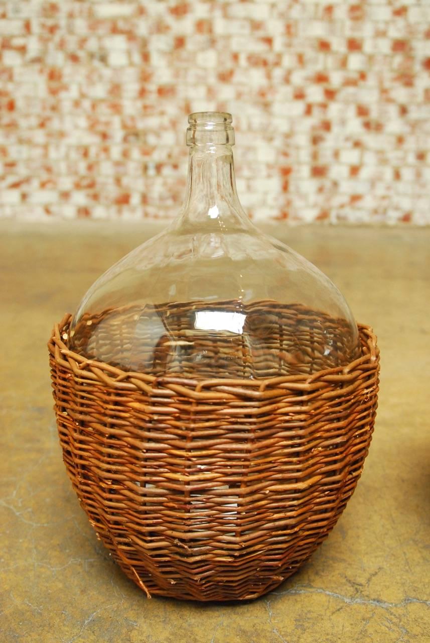 Matching pair of wine carboy or demijohn glass bottles featuring a woven willow reed cover. French style with large bulbous form.