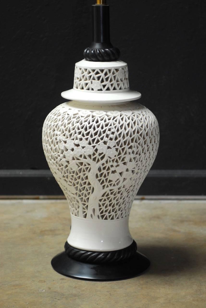 Large Mid-Century Modern Chinese blanc de chine porcelain table lamp in the form of a ginger jar vase. Featuring a pierced fretwork body of cherry blossom trees with a matching lid. Mounted on an ebonized wood base with brass hardware. Unusual large