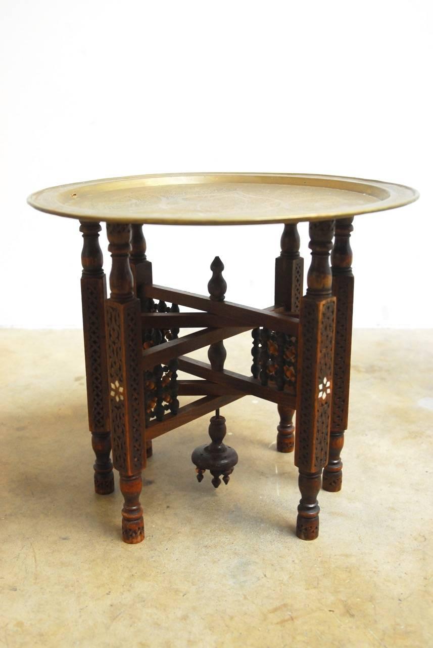 Handsome Middle Eastern folding tabouret brass tray drinks table featuring a six-leg folding base. The intricately carved base has bone inlay on each leg and attaches to a turned centre column ending with finials. Topped with a brass tray showcasing