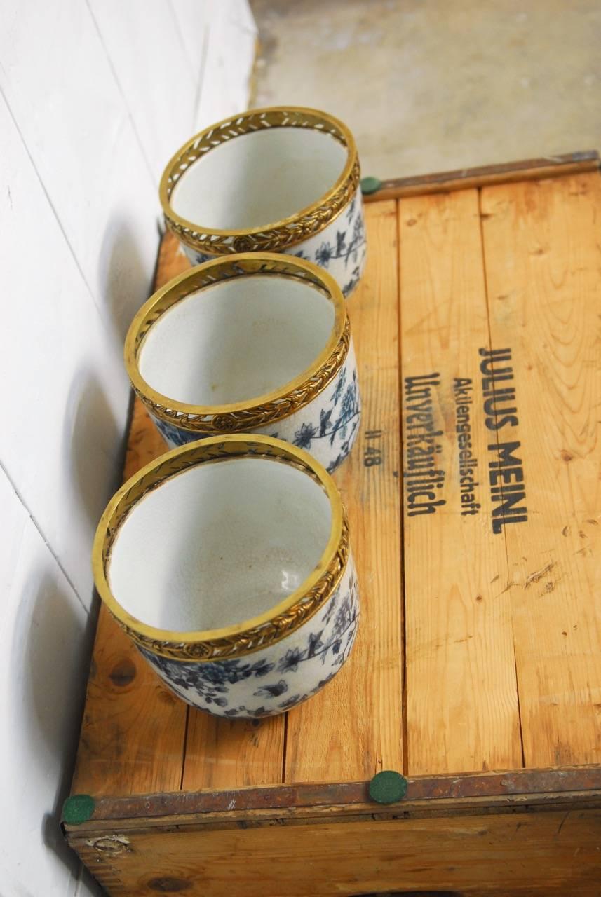 Stately set of three Chinese blue and white porcelain urns or vases featuring decorative brass mounted rims. Each pierced with a floral and foliate motif brass top. The urns have a beautiful glaze with a craquelure finish and are decorated with