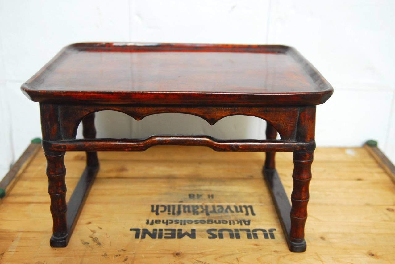 Diminutive Japanese lacquered tray table or serving table made from carved wood. Features a galleried top tray with scalloped sides for handles and humpback stretchers. Supported by faux bamboo carved legs. Perfect size to hold a laptop or use as a