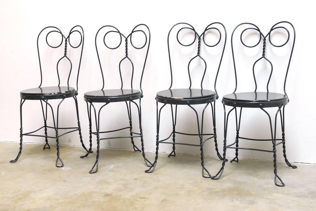 Charming set of four French bistro chairs or ice cream parlor chairs made of iron. Features a round wooden seat that has been lacquered in black. The frames are constructed from thick, hand-crafted twisted iron conjoined to a round seat. Wooden seat
