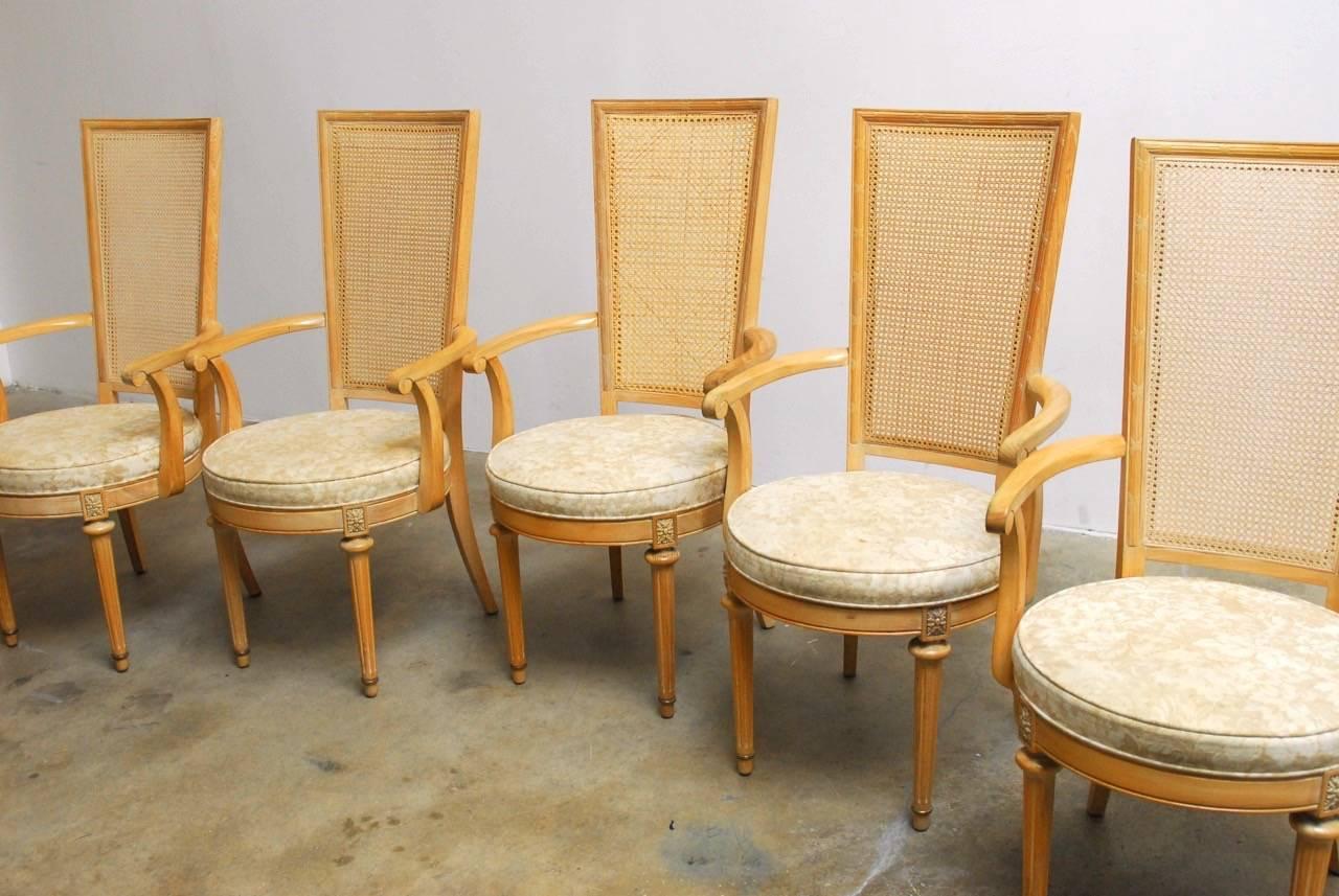 Rare and unusual set of five Louis XVI style caned dining chairs. Featuring a tall square caned back contrasted by a round seat. The back is decorated with neoclassical accents and the seat has carved rosettes on the apron. Supported in front by two