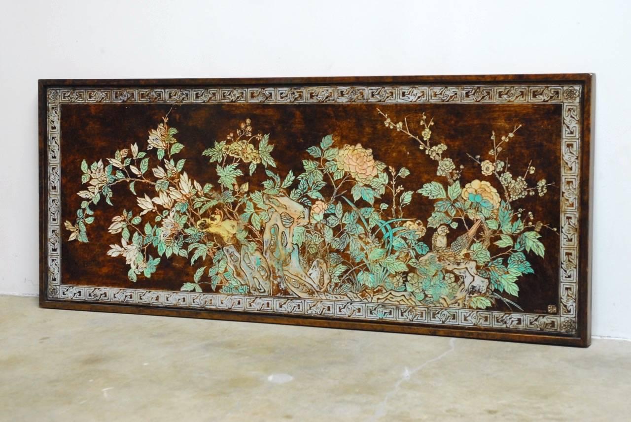 Colorful Chinese floral and foliate painted relief panel. Features an abundance or verte colored leaves with flowers and birds over a brown background. Bordered with a geometric carved design finished in a light shade. Signed and sealed on bottom