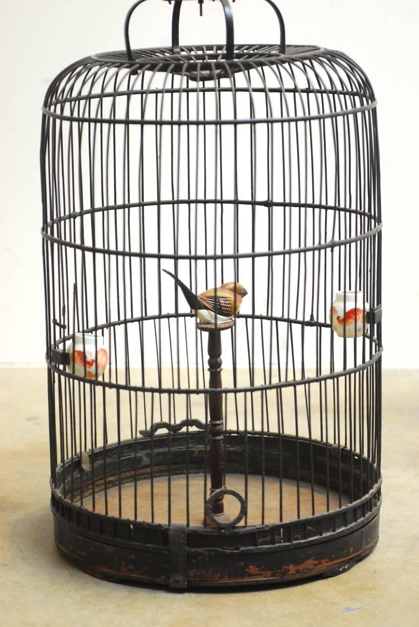 Impressive antique Chinese domed bamboo birdcage with a functioning sliding door. Features a dark lacquer finish and a decorative brass metal Phoenix hook formed from its tail. Made in the Chinese Art Deco taste, this beautiful cage has a pedestal
