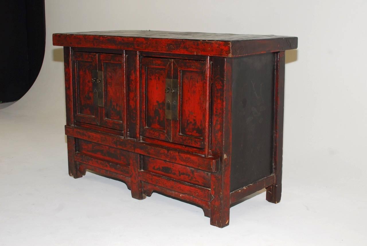 Rustic 19th century Chinese provincial coffer featuring a thick distressed red lacquer finish. The cabinet is fronted by two sets of doors opening to a two shelf interior. Produced from antique wood having wooden hinged doors. The top panel has dark