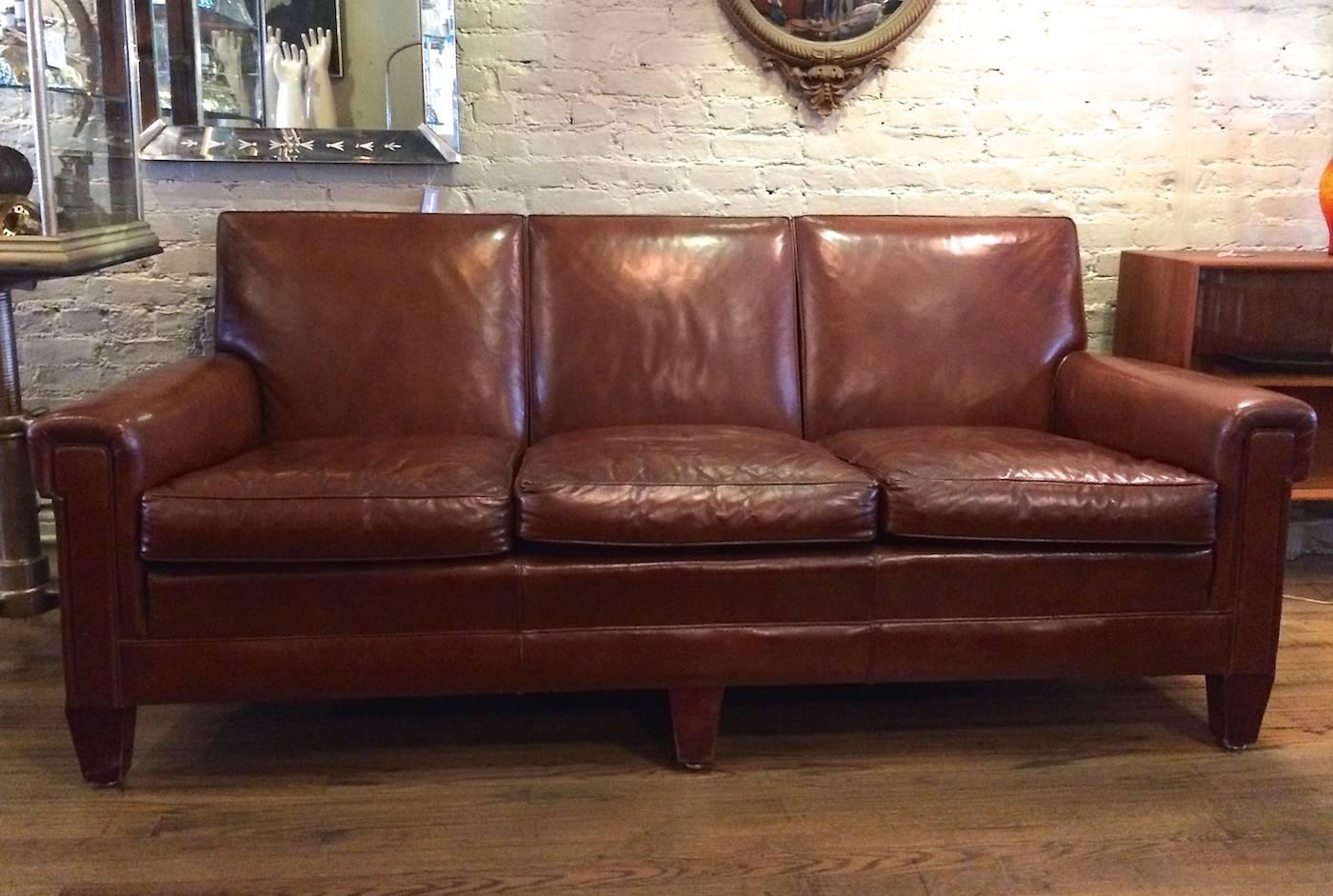 Stately club sofa in a rich cognac brown leather with mahogany legs by The Sikes Company of Buffalo NY. Solid, American, Mid-Century construction, circa 1940s.