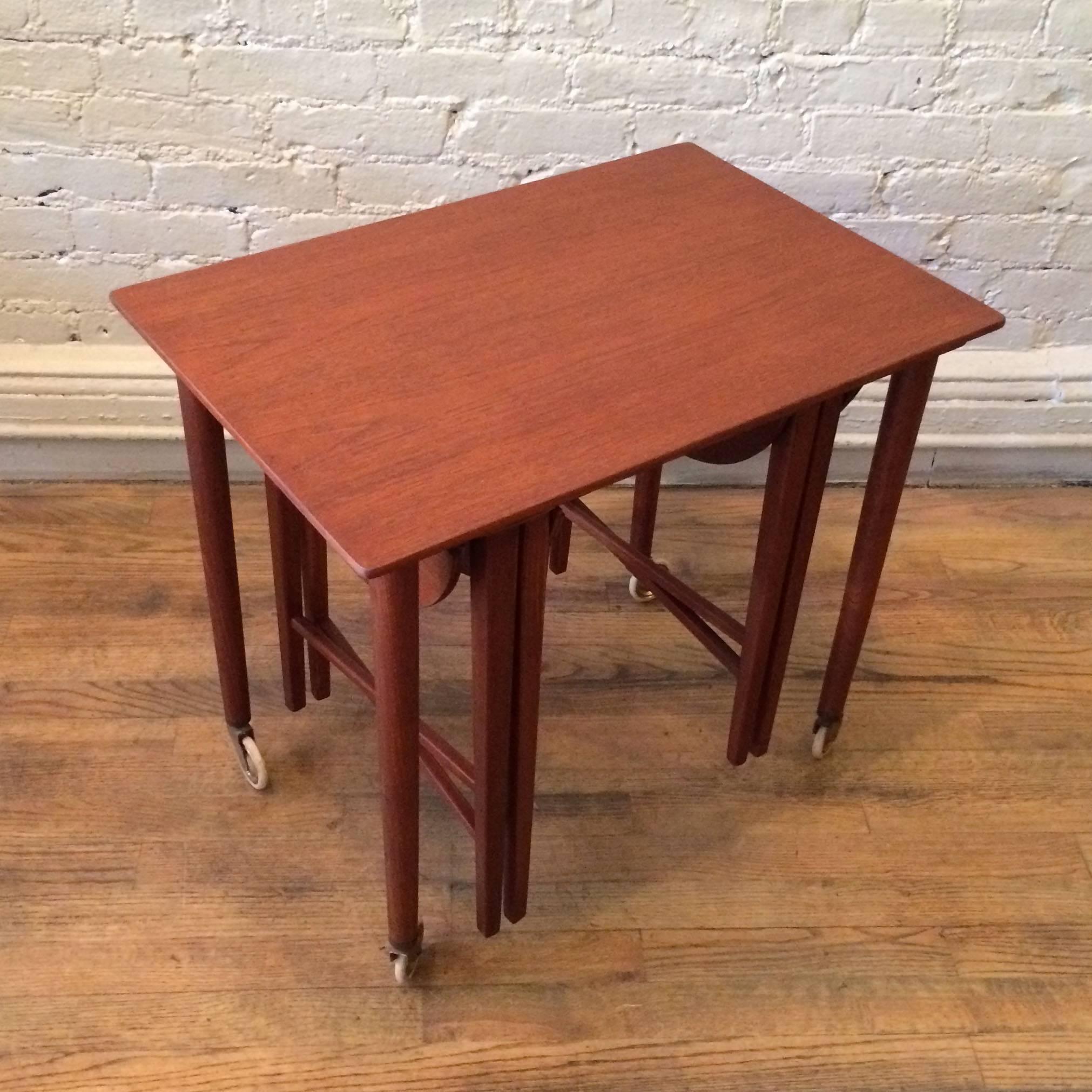 Set of three Danish modern, teak, nesting tables attributed to Grete Jalk has one rolling rectangular table with two folding round top tables that suspend stored under carriage.

Overall dimension is 24