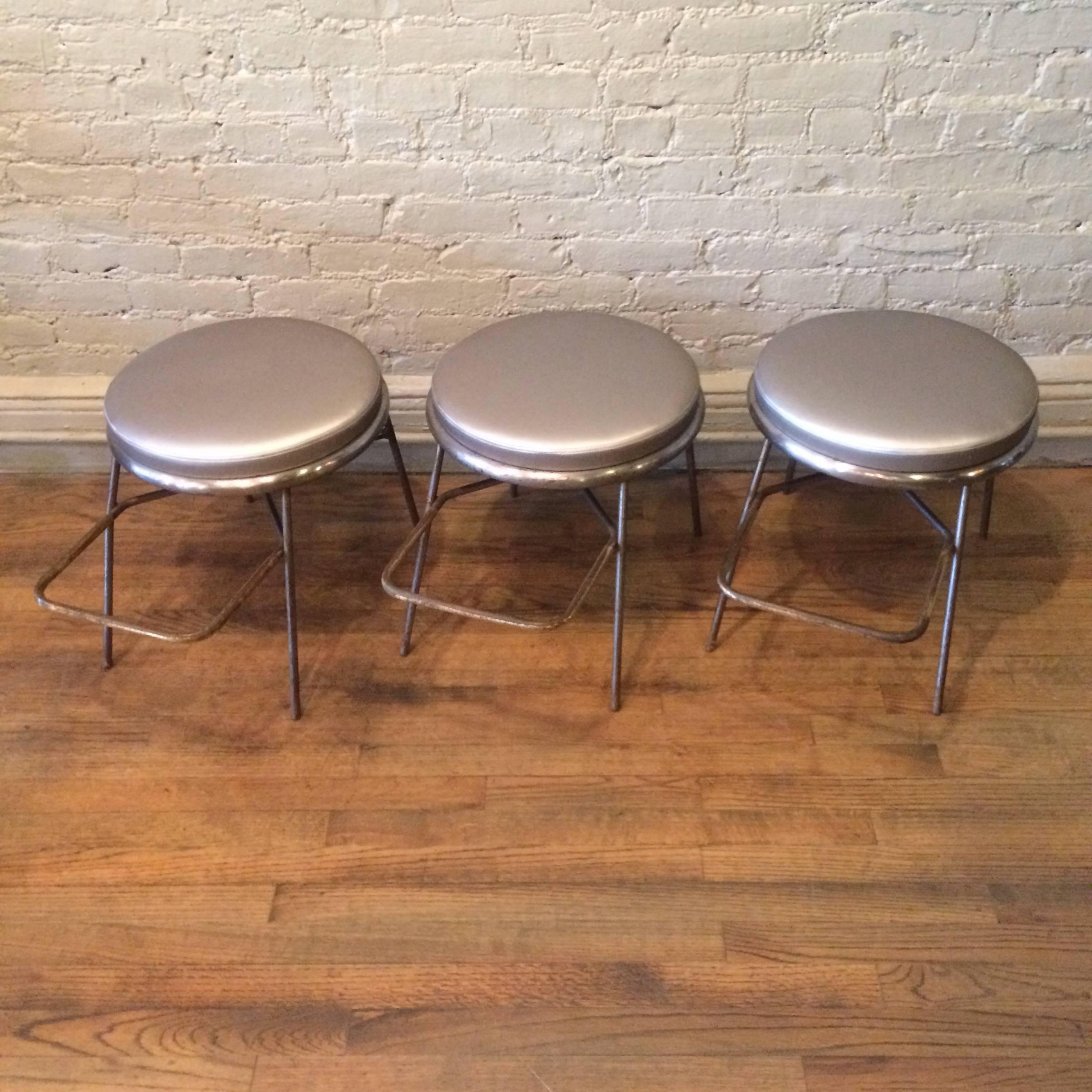 Midcentury, shoe store, fitting stools feature patinated, brushed steel frames with brass-plated footrests and newly upholstered silver vinyl seats. Two stools are available, sold individually.
 