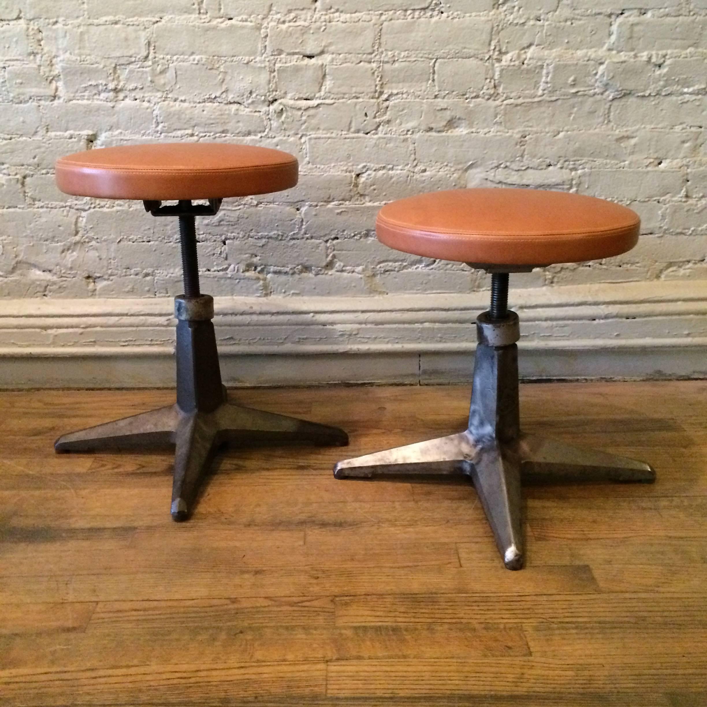 Industrial, cast iron, star base stools with newly upholstered tan leather seats are height adjustable from 12 - 19