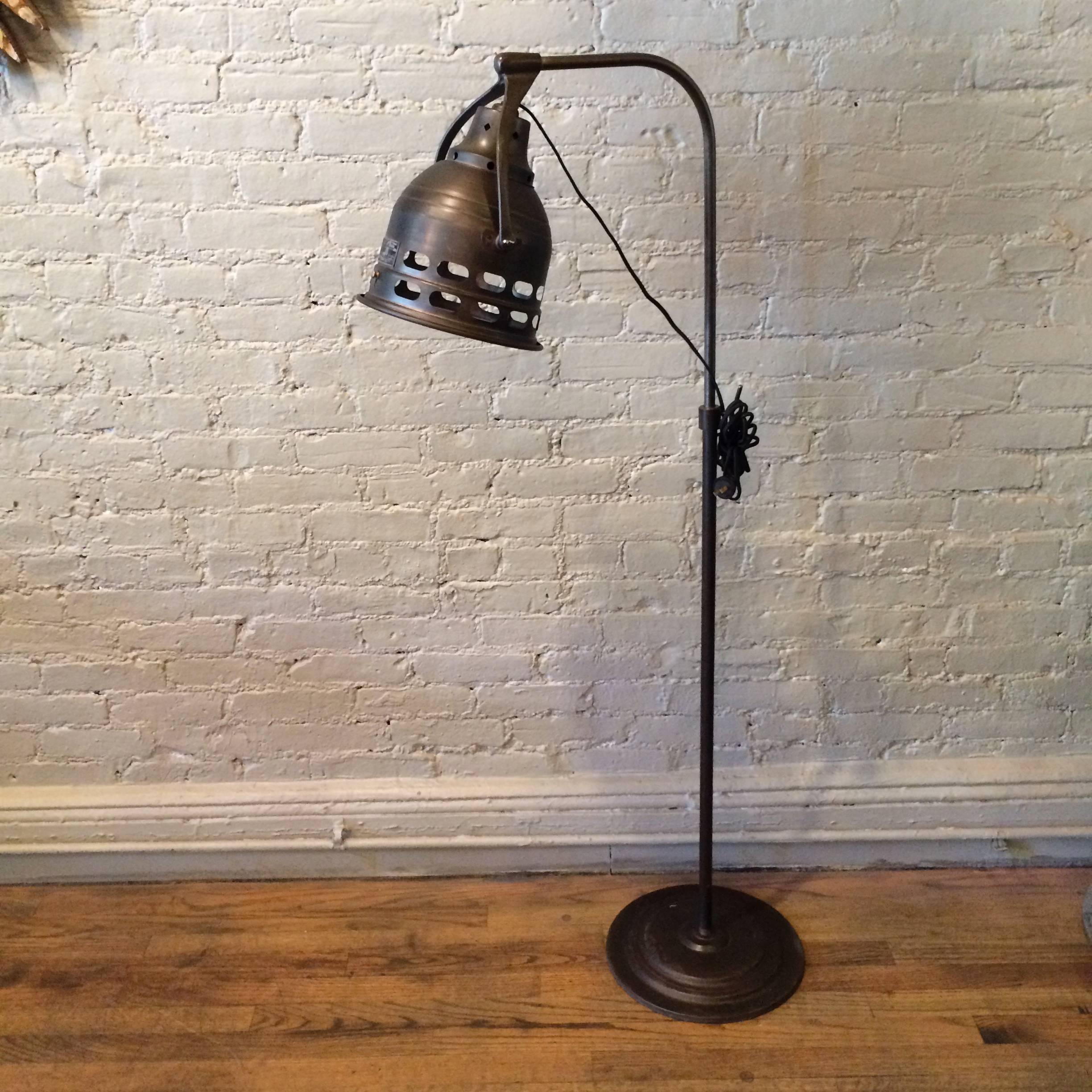 Vintage, 1920s, steel, adjustable height, medical floor lamp in a gunmetal finish features a weighted base and articulating head with Fresnel glass lens insert. Lamp takes a regular bulb up to 200 watts.