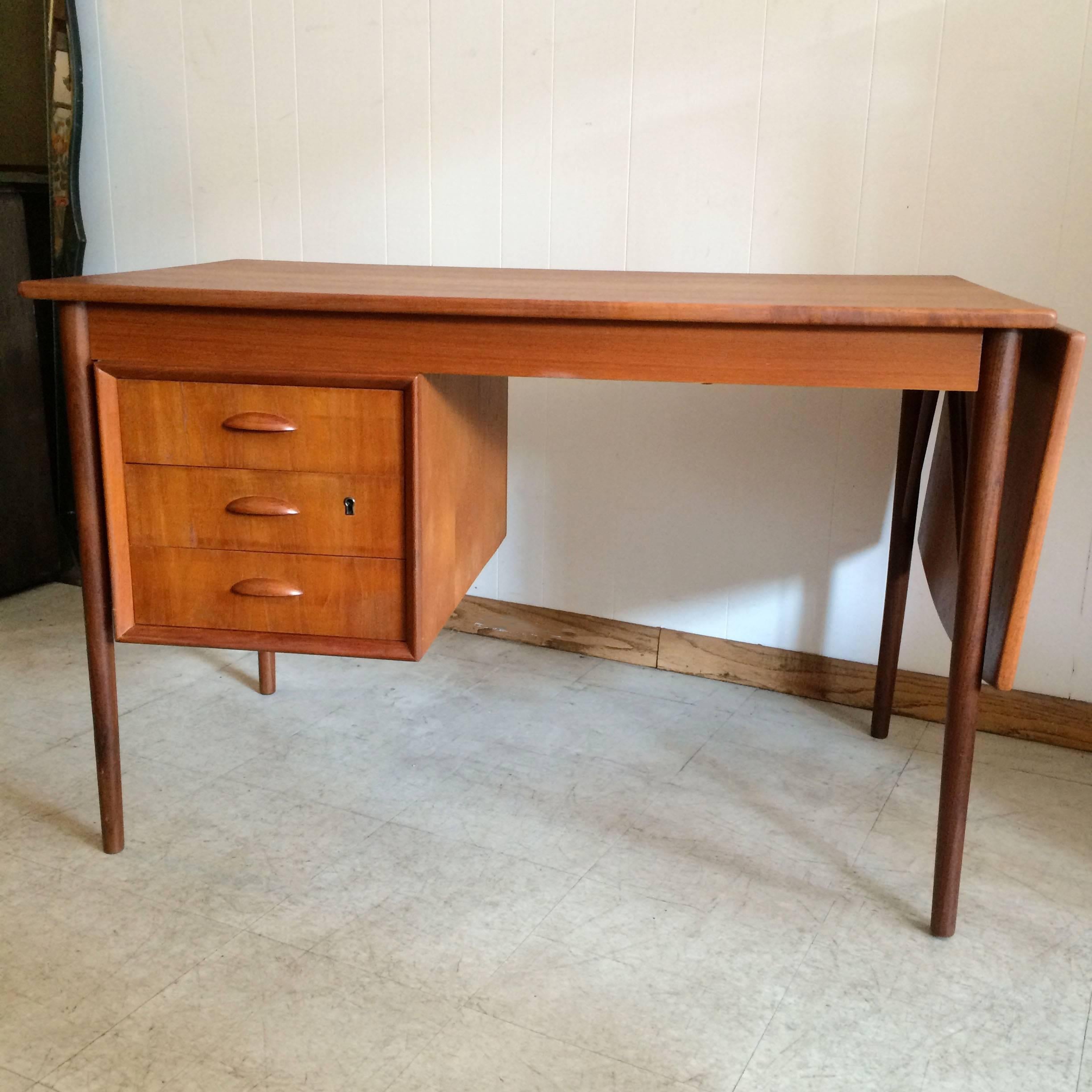 Danish modern, teak desk with drop leaf extension is finished in the back with a display bookshelf. Wonderful details include tapered legs, curved drop-leaf edge and cup pulls. Marked made in Denmark. Desk extends from 47