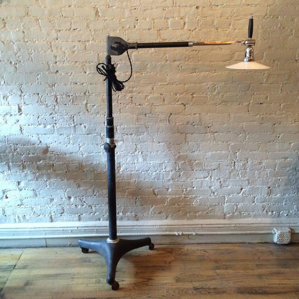 Industrial, articulating, dentist floor lamp, circa 1920s has an adjustable, rolling cast iron base and telescopic, chrome arm with articulating task head with stained walnut grip. A milk glass disc shade has been added for ambient, diffused light.
