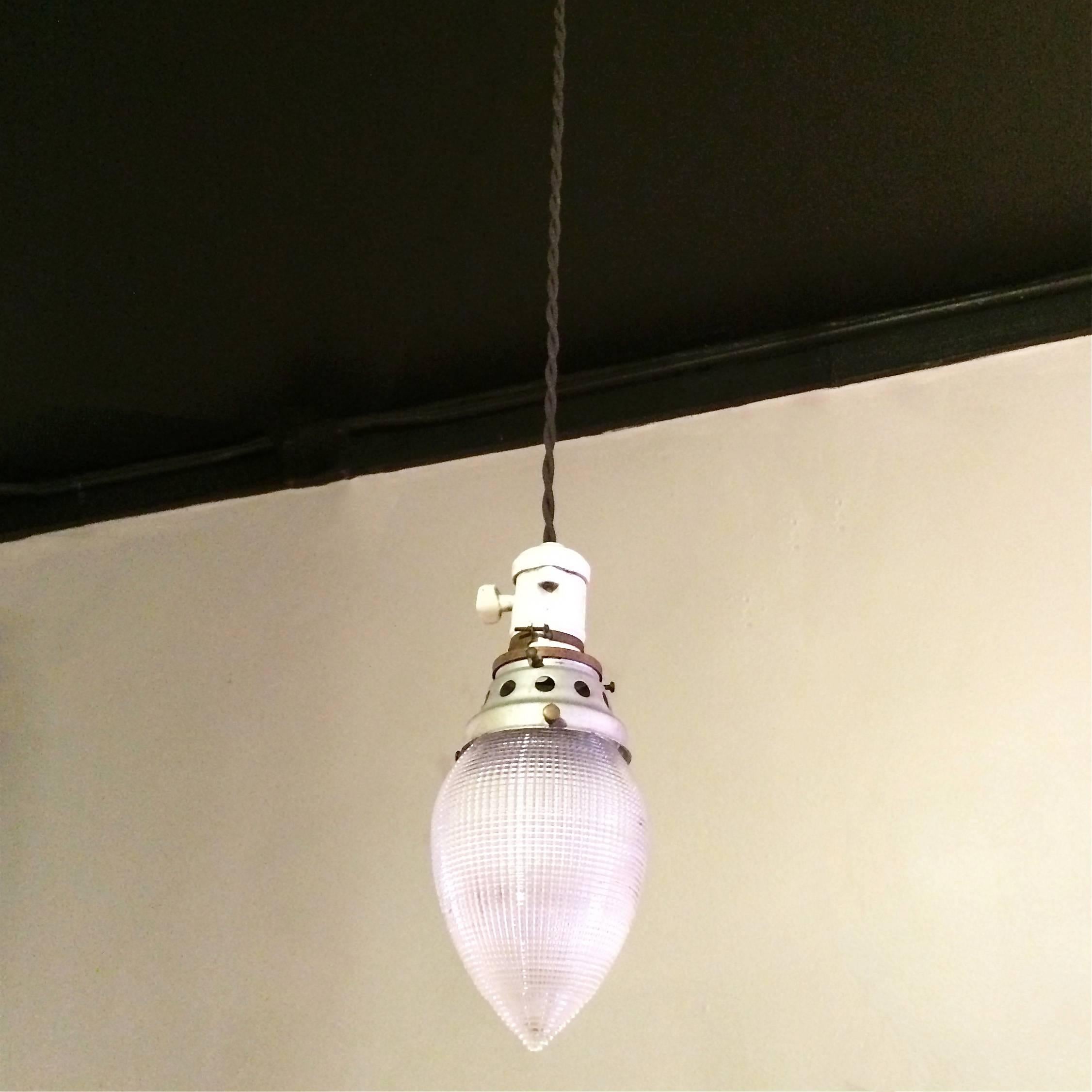 Industrial, teardrop shape, Holophane glass, pendant lights featuring porcelain sockets with paddle switches and steel and brass fitters are newly wired with 42in. of brown braided cloth cord. Two more teardrop pendants are available with slightly