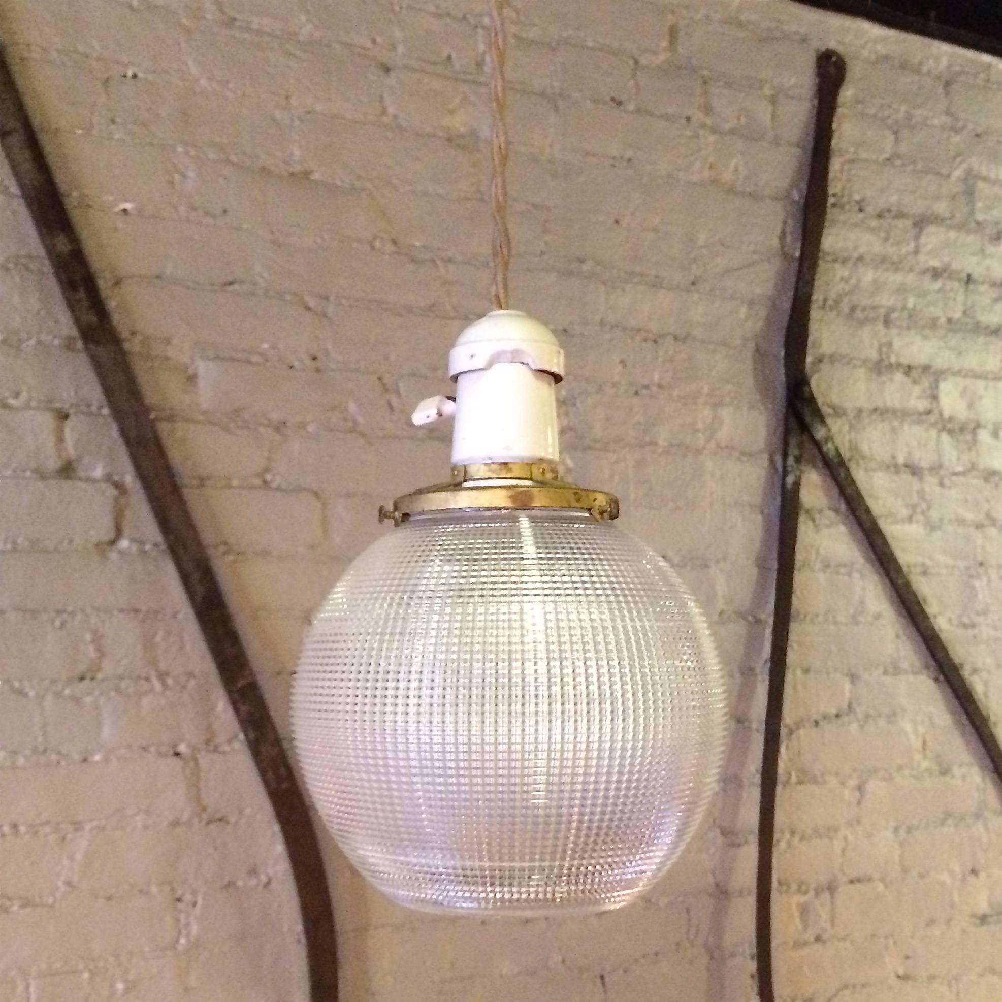 Pair of holophane glass, open globe, pendant lights with porcelain sockets and brass fitters are newly wired with 50in. of beige braided cloth cords. Each pendant can take up to 150 watt bulbs.