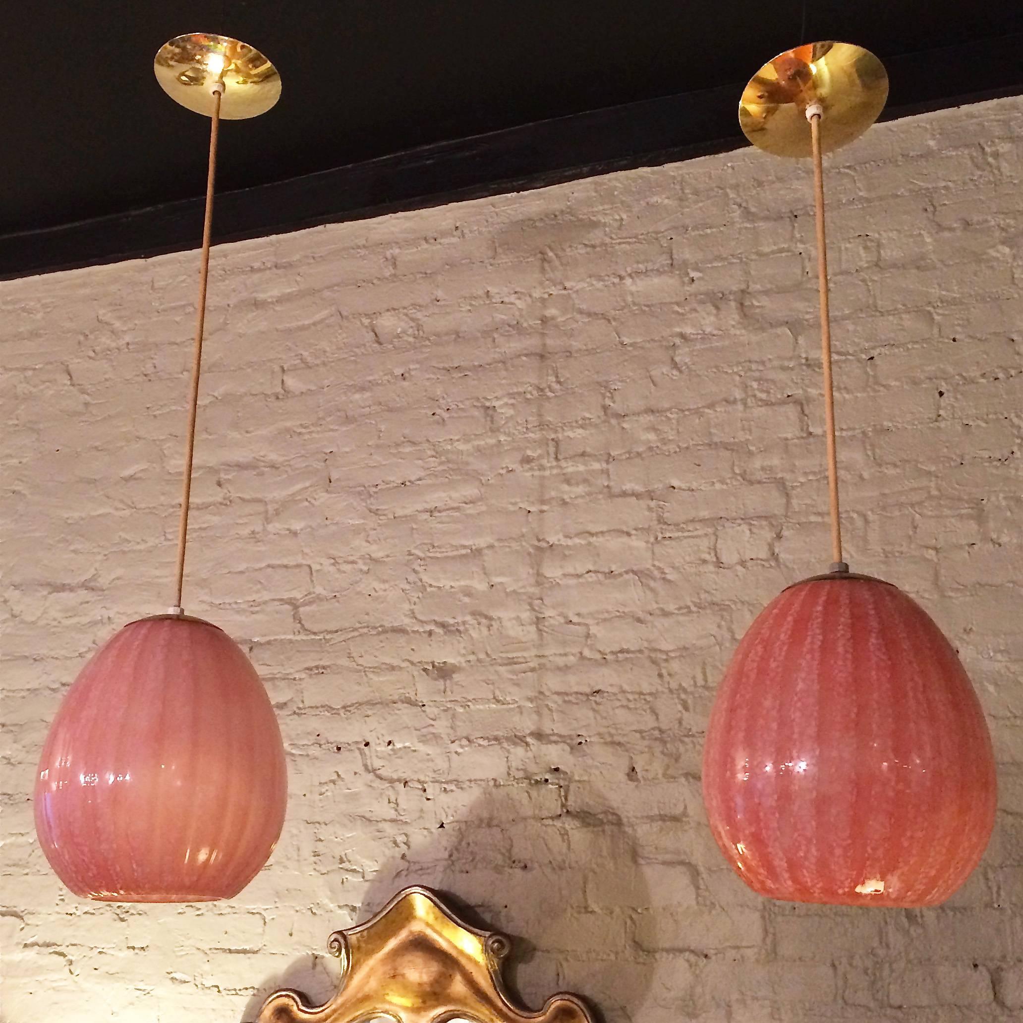 Pair of Hollywood Regency pendant lights with pink, blown glass shades with open bottoms. The pendants are wired with cloth cord that hang 38