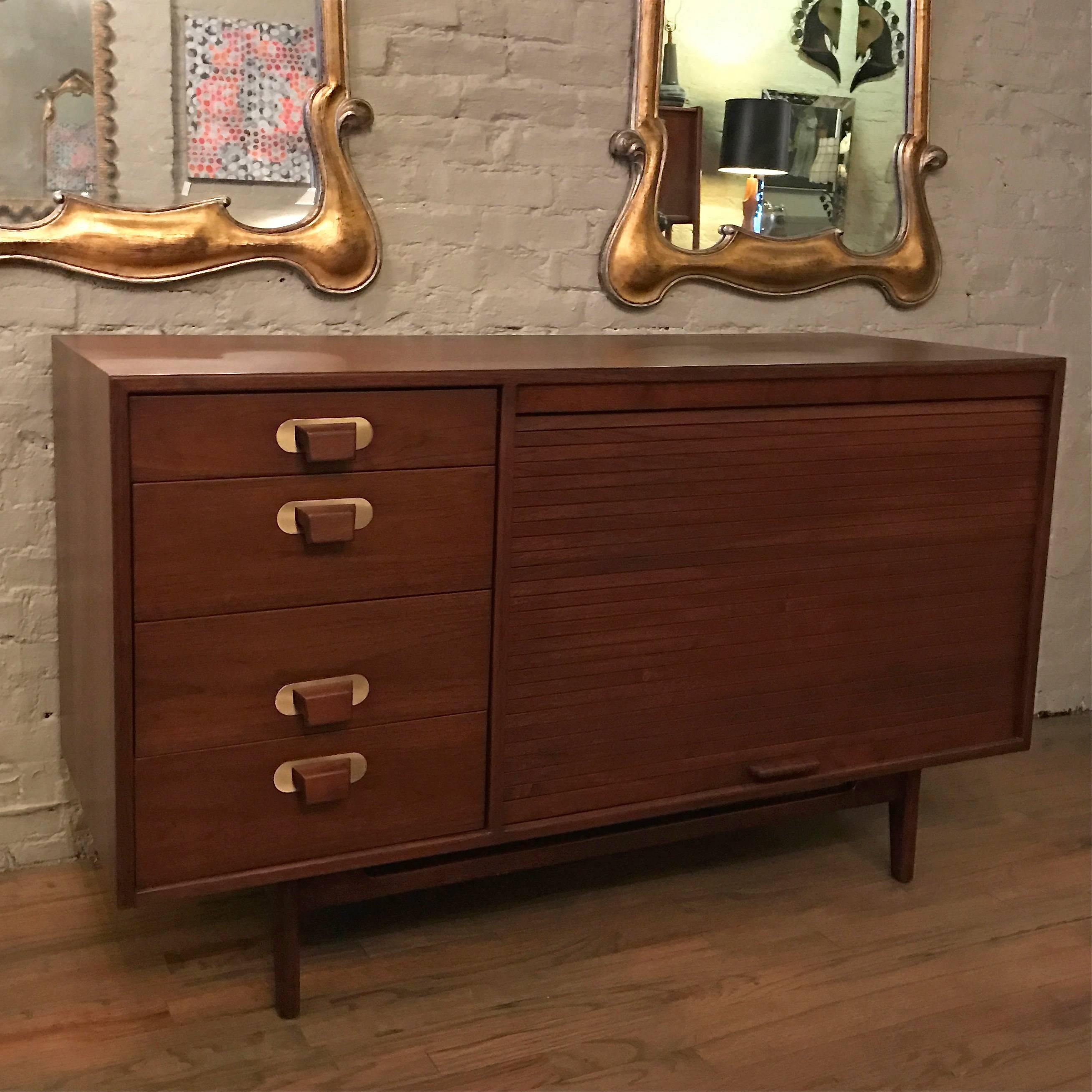 Early, Mid-Century Modern, compact, walnut credenza by Jens Risom featuring a tambour front concealing shelving and four side drawers with brass accented pulls.