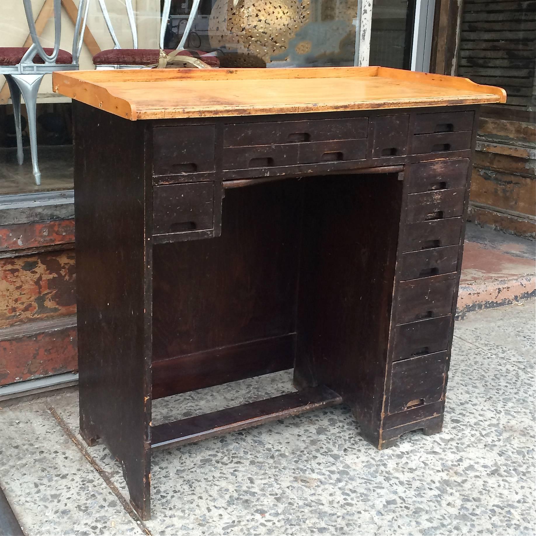 Industrial, maple, watchmaker’s desk with 15 drawers of various size has a wonderful, work-worn patina. There is also a framed canvas ledge that pulls out below the centre drawers to catch small parts. It functions as a tall desk, console or kitchen
